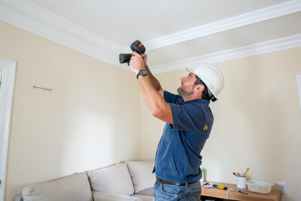 Carpenter fitting and caulking crown molding in an Atlanta, GA living room